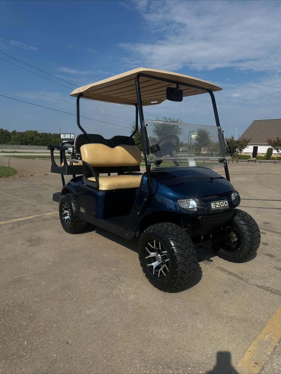 Black golf cart parked on a concrete surface under a clear sky.