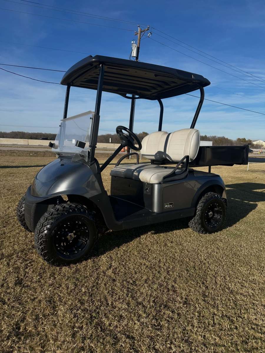 Silver golf cart with beige seats parked on grass under clear sky.