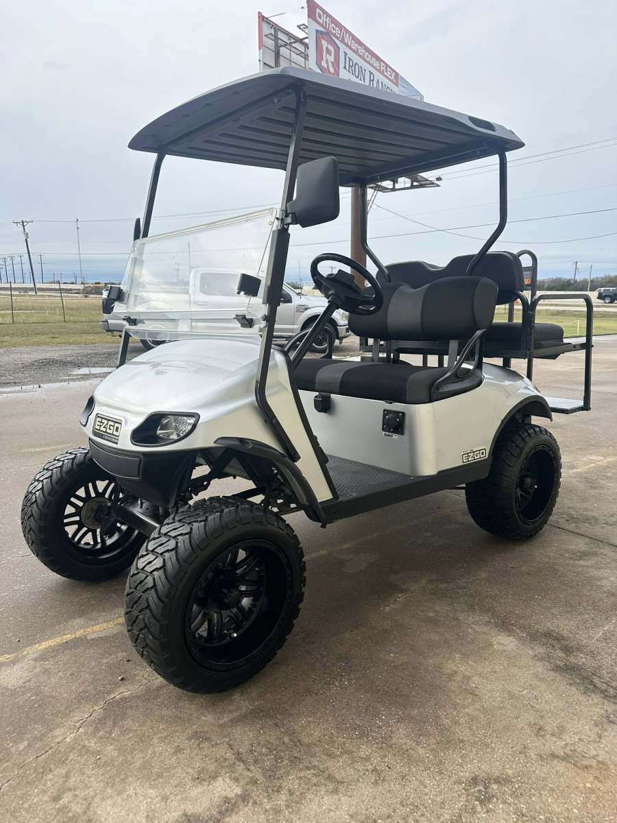 White golf cart with lifted suspension and black roof parked on concrete.