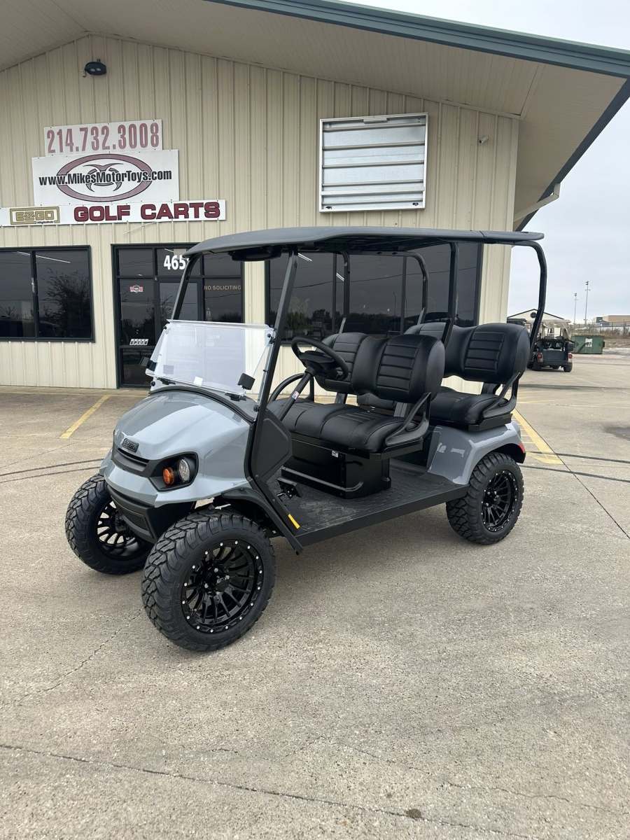 A silver golf cart with black seats and rugged tires parked outside a building.